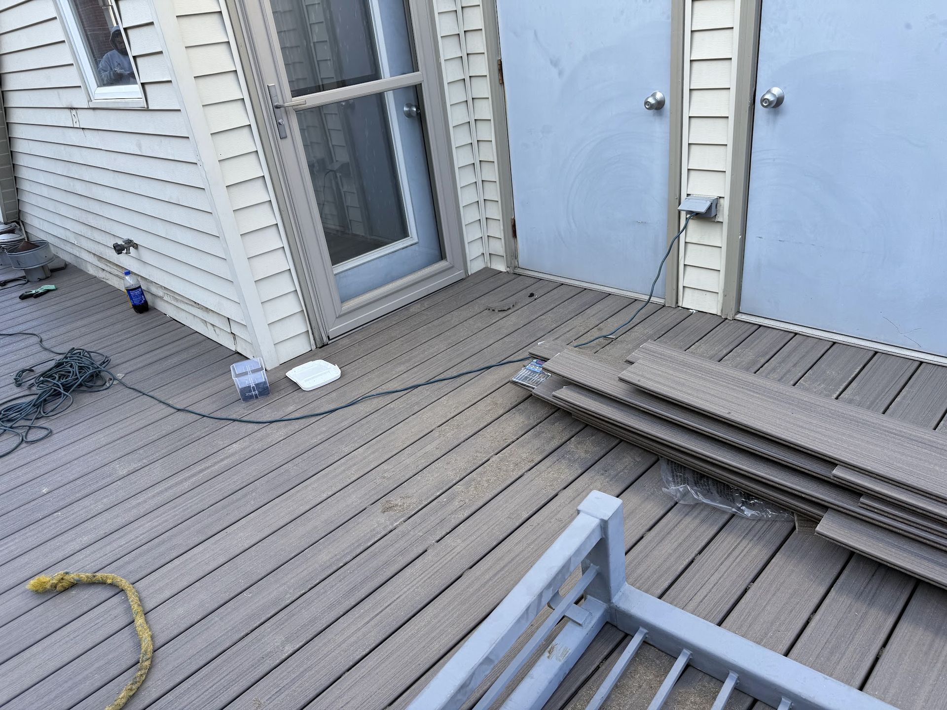 Wooden deck beside a white house, with stacked boards, a blue door, and a hose on the left.