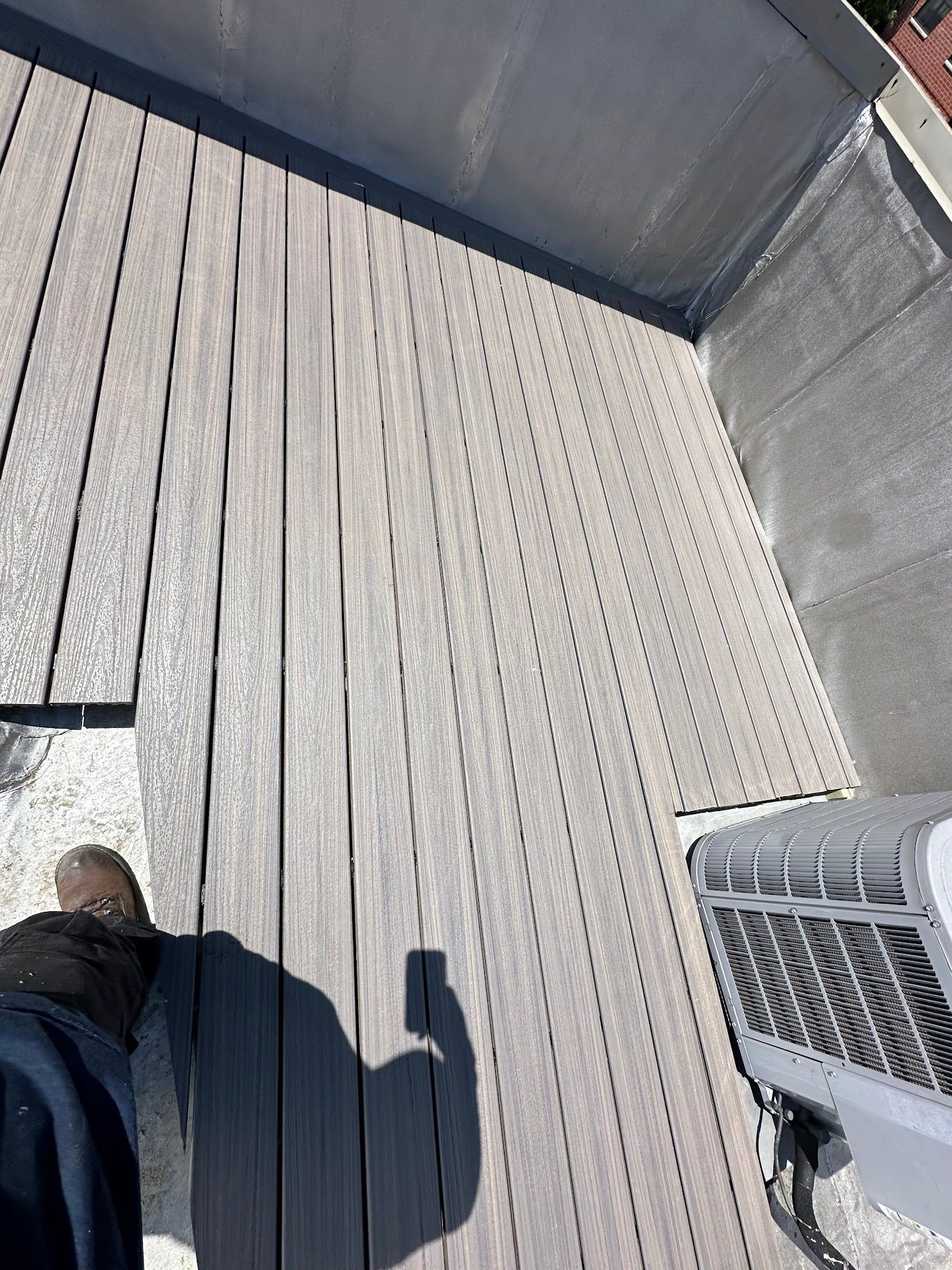 View from a height onto a sunlit wooden deck, with a person's foot and metal railing visible.