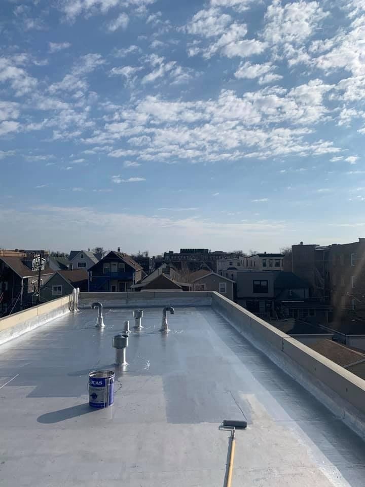 Rooftop under construction with reflective coating, tools, and a cloudy blue sky over nearby houses.