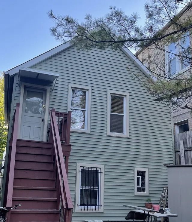 Gray house exterior with maroon stairs, barred window, and pine branches overhead