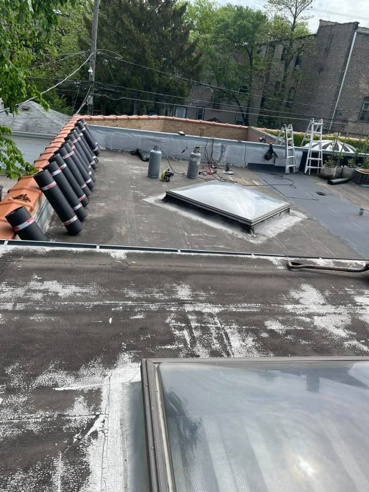 Rooftop with worn black membrane, skylight, vents, and stacked black panels along the edge