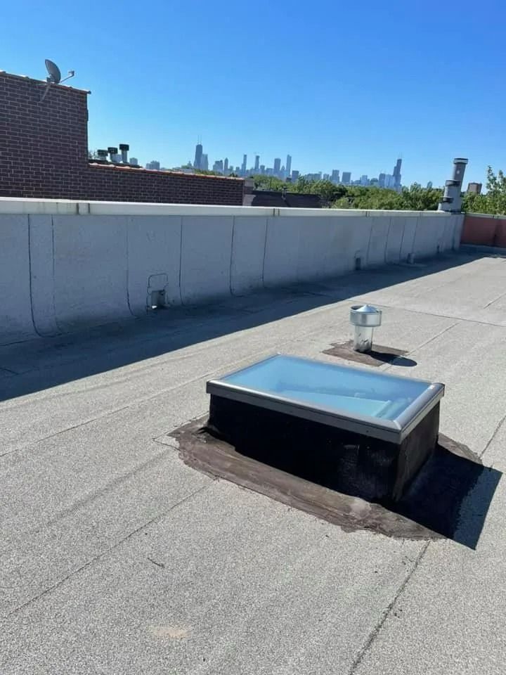 Rooftop with a skylight vent and city skyline under a clear blue sky.