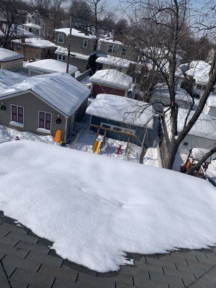 Snow-covered rooftops and backyard sheds in a residential neighborhood, viewed from above.