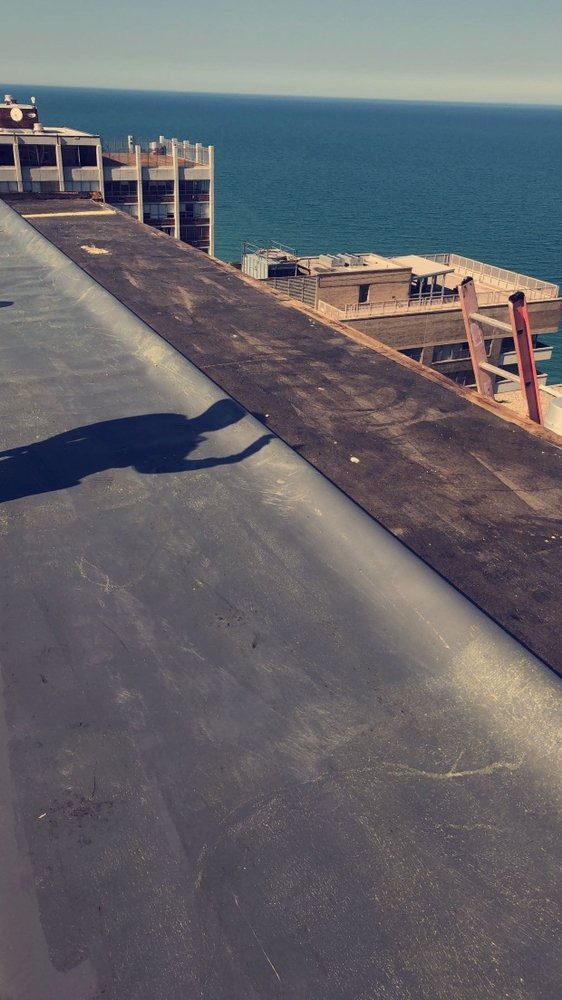 Rooftop walkway overlooking the ocean, with a concrete roof edge and blue sky.