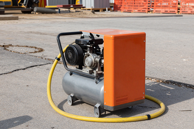 Portable air compressor unit on a paved job site with pneumatic hose — compressor rental Indianapolis Indiana