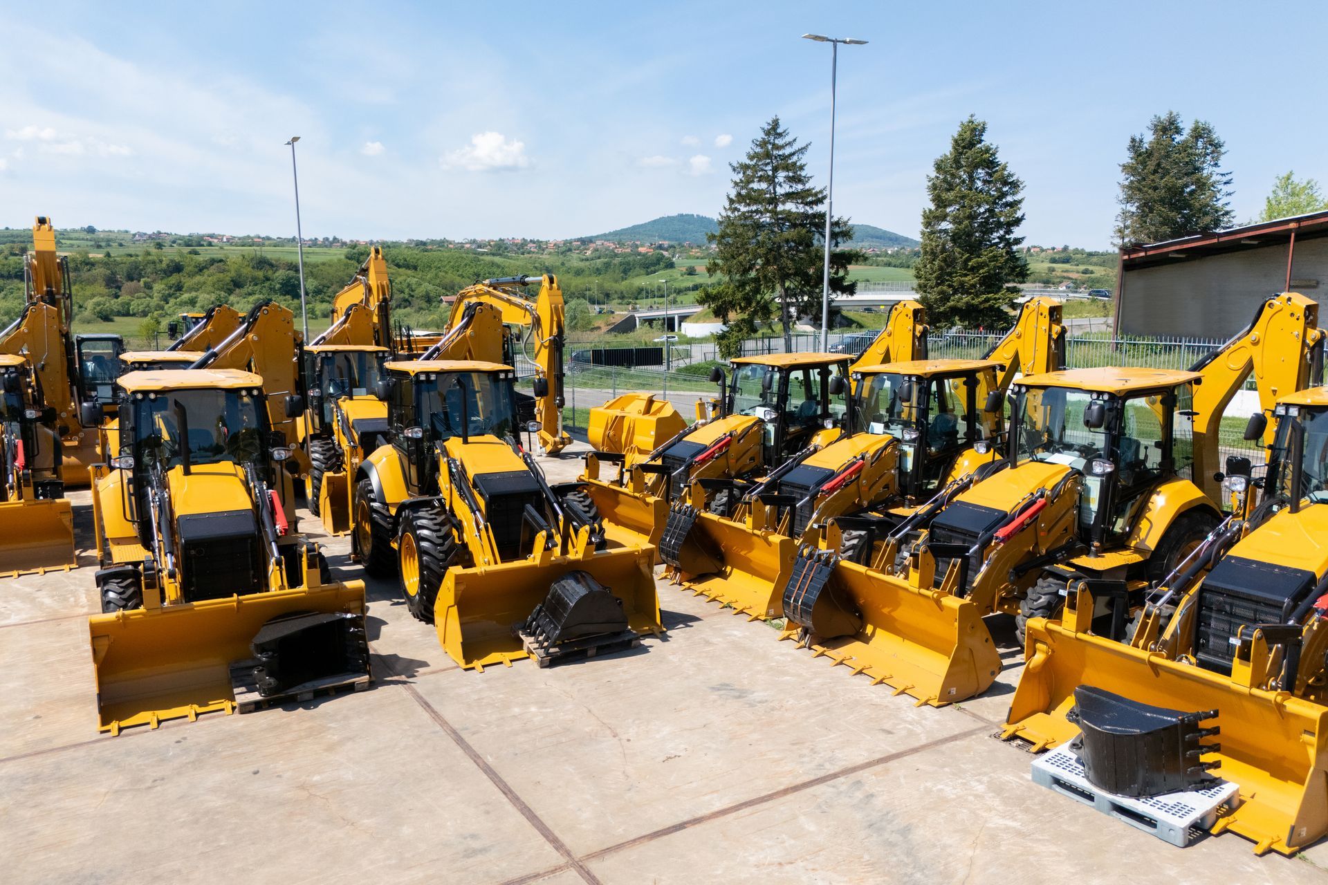 Rows of yellow backhoe loaders and excavators parked in an outdoor construction equipment yard.