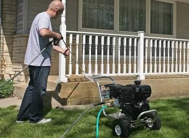 Yellow pressure washer spraying water onto a stone patio in a garden.