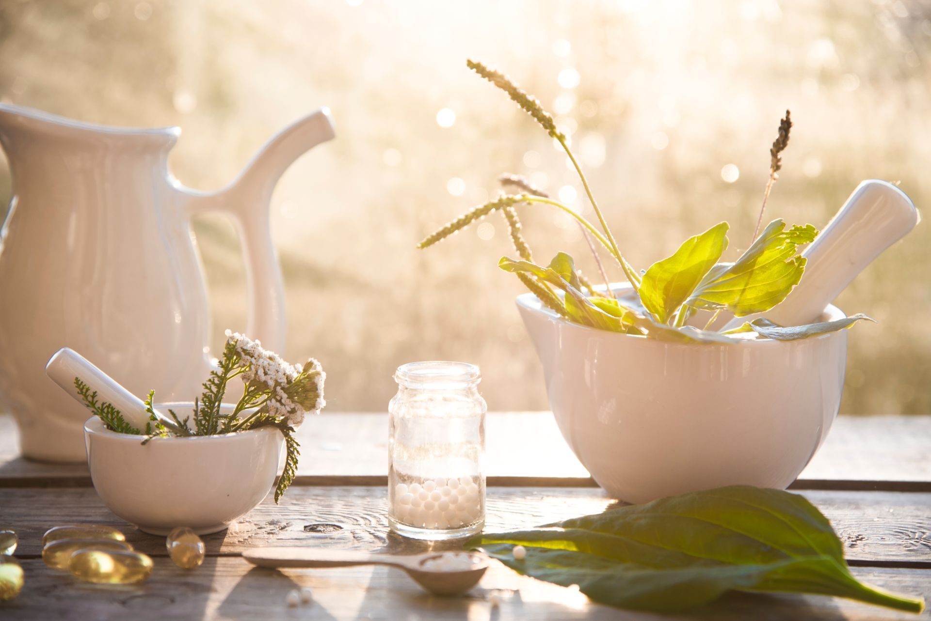 Sunlit herbal tea setup with white pitcher, bowl, and glass jar on a rustic table