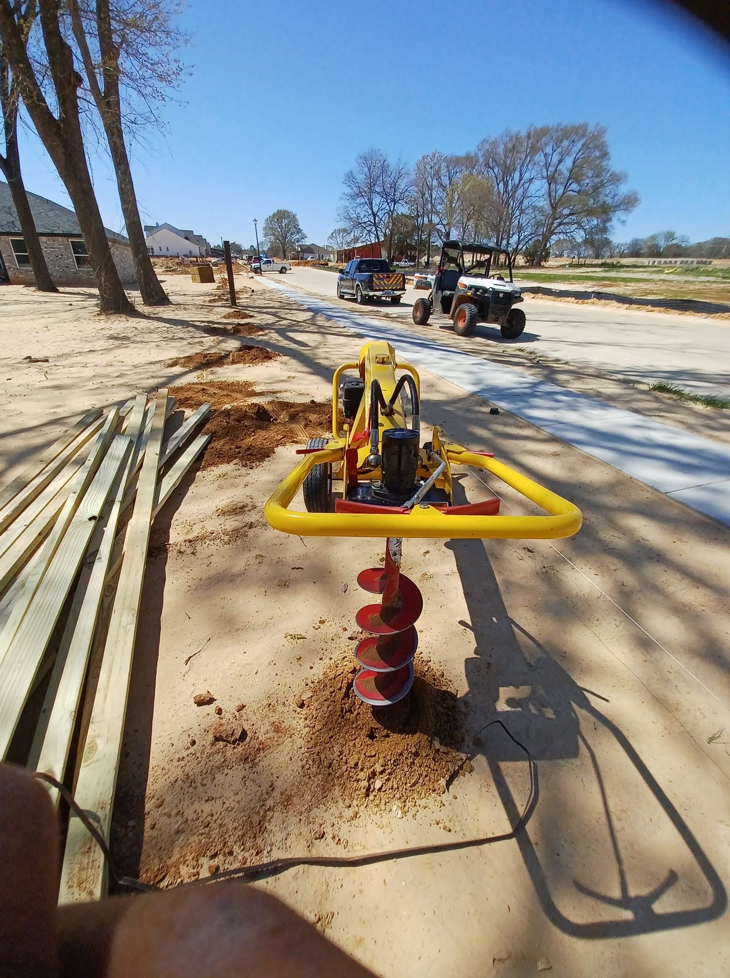 Yellow ground auger drilling beside a sandy construction road with equipment in the distance