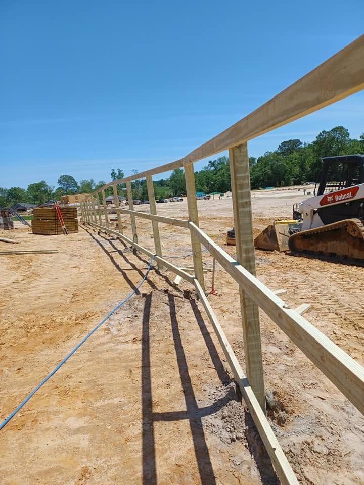 Construction site with a long wooden rail along a dirt path beside heavy equipment under a blue sky