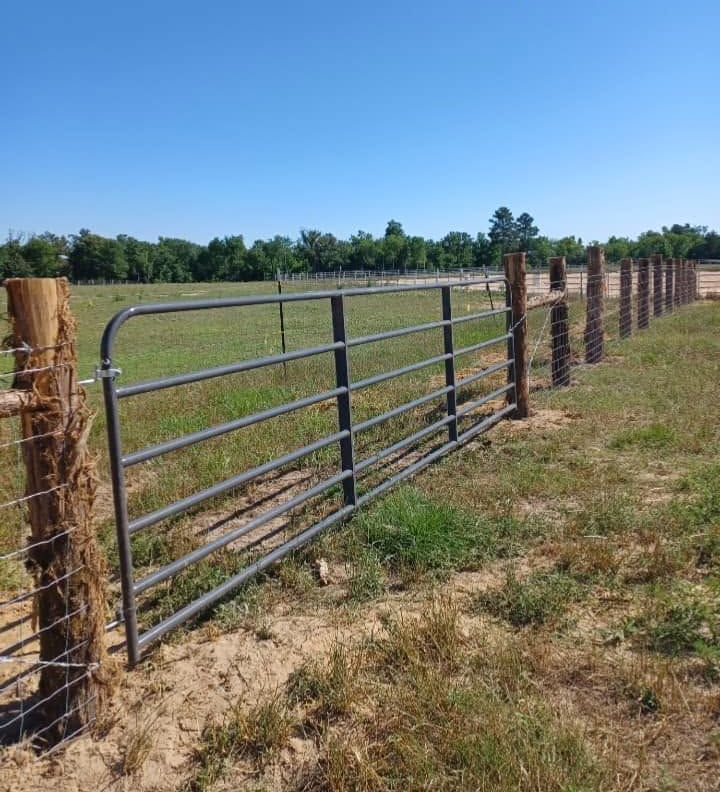 Metal ranch gate and fence along a dry field under a blue sky
