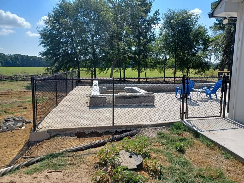 Backyard patio with a fenced concrete area, picnic table, blue chairs, and a grassy yard beyond.