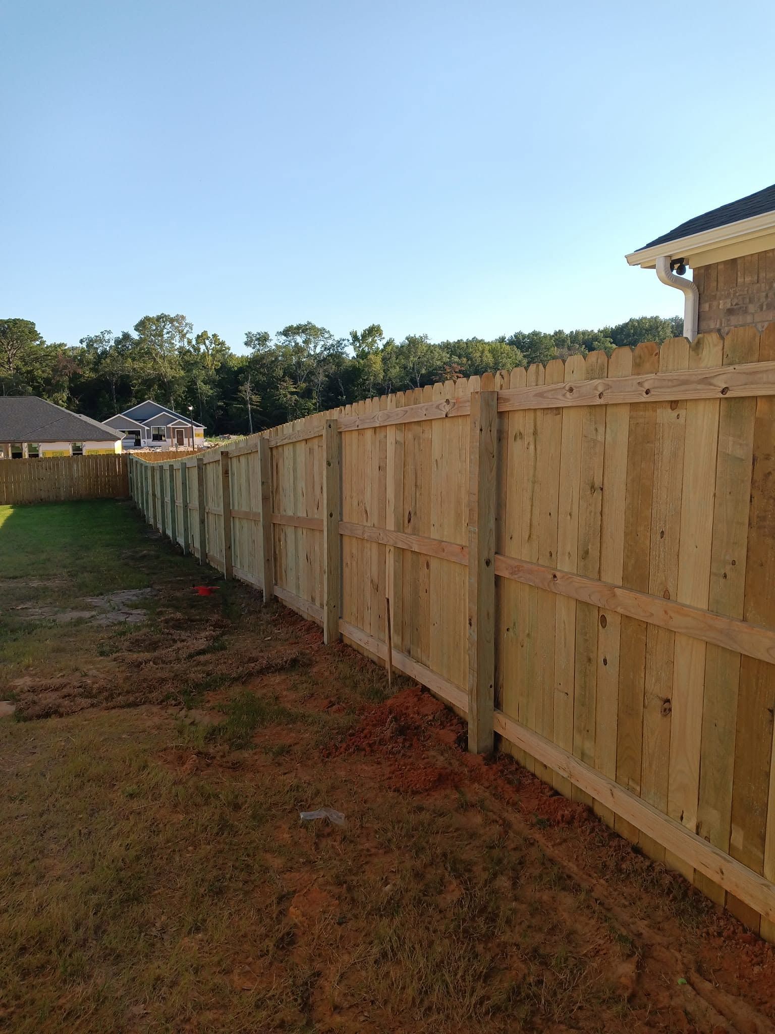 Long wooden privacy fence along a grassy backyard beside a house at sunset