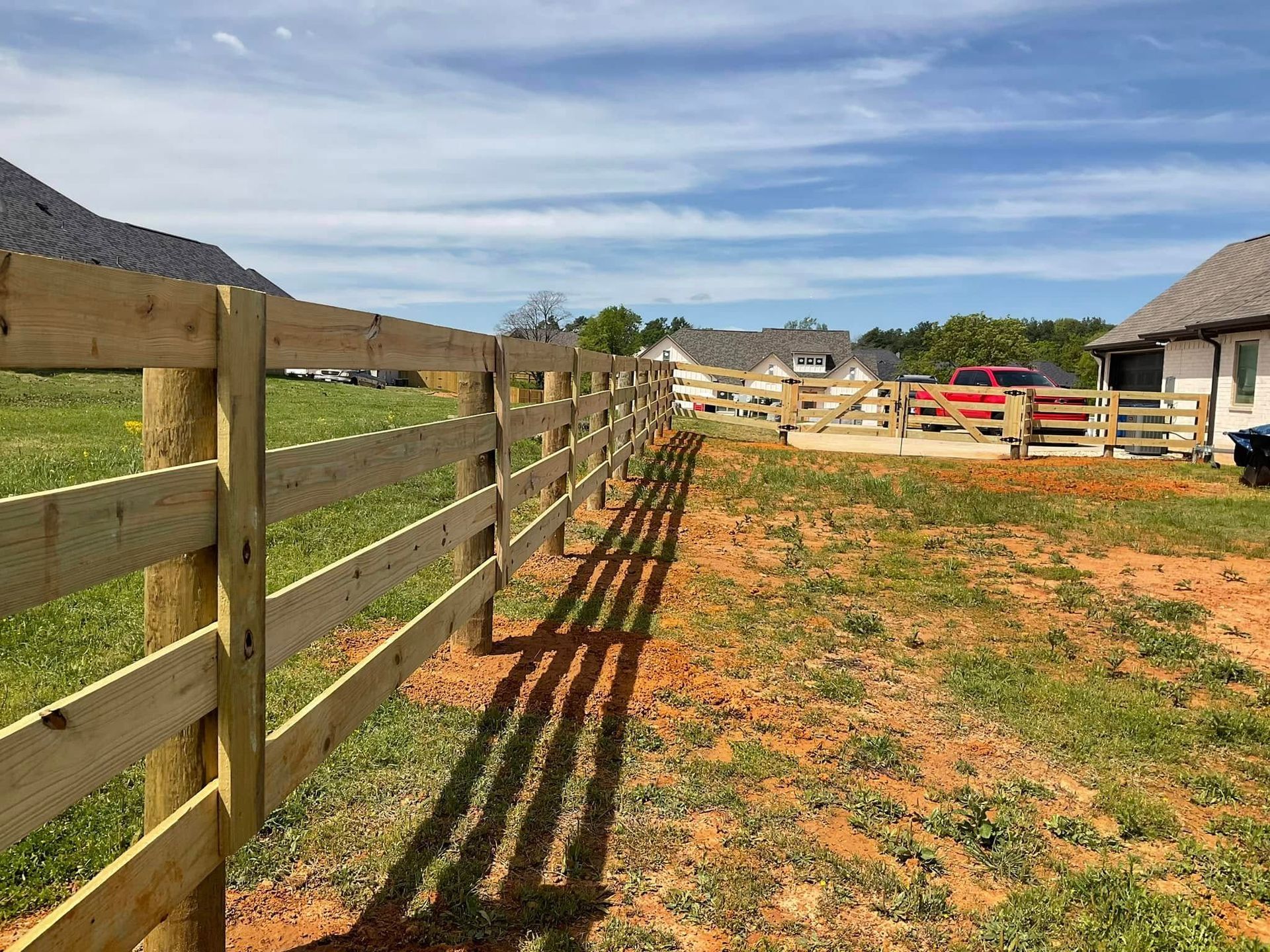 Wooden fence beside a dirt path in a rural yard, with houses and mountains in the background