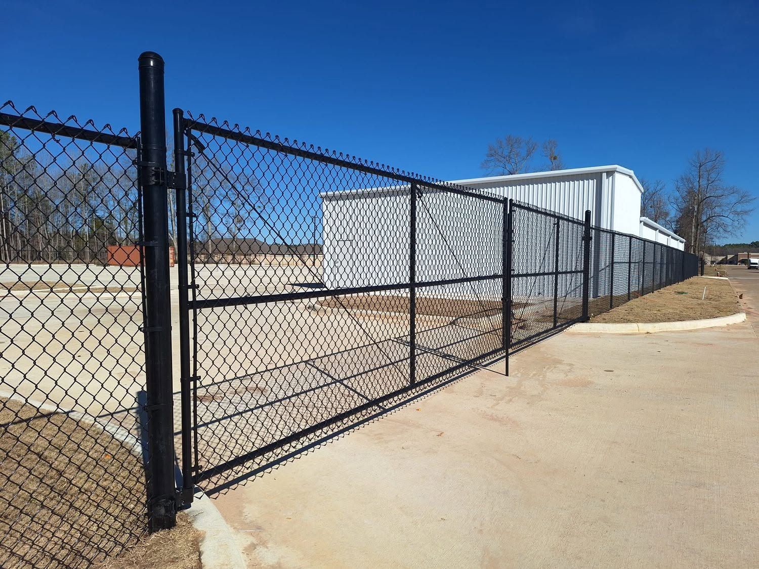 Chain-link fence beside a white industrial building under a clear blue sky.