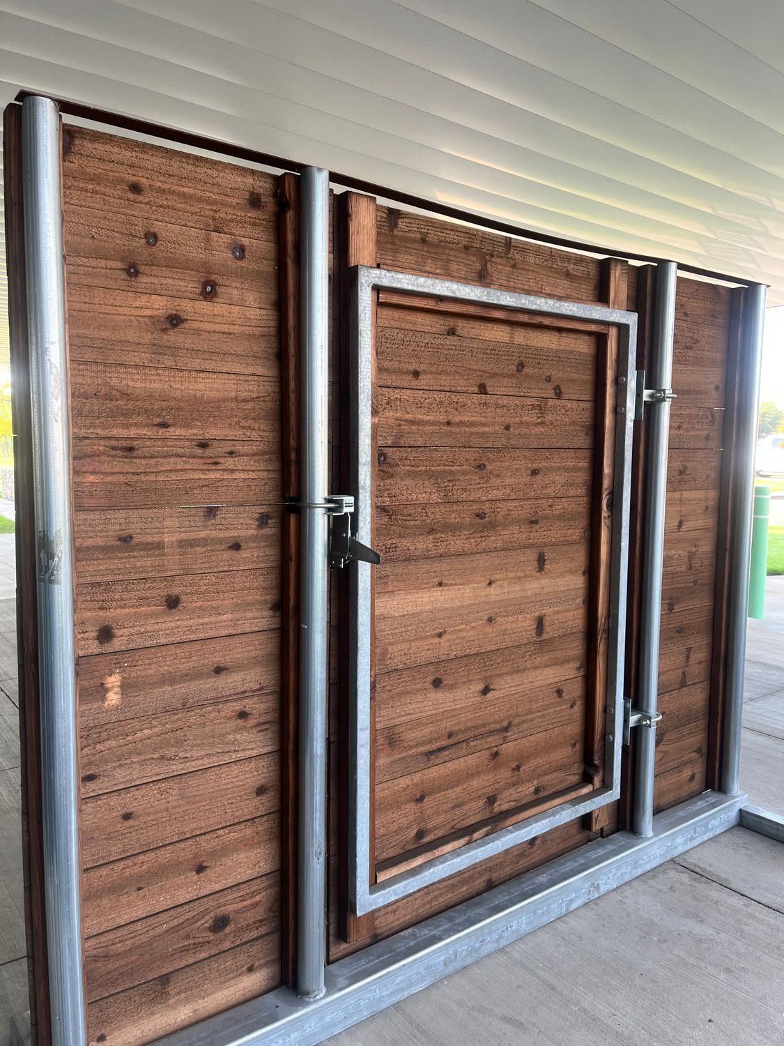 Wooden barn-style wall panels with a small framed door and latch under a covered porch.