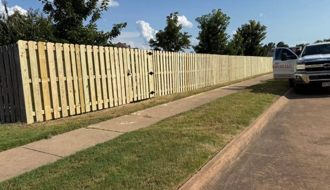 New wooden fence enclosing a grassy backyard with trees in the background