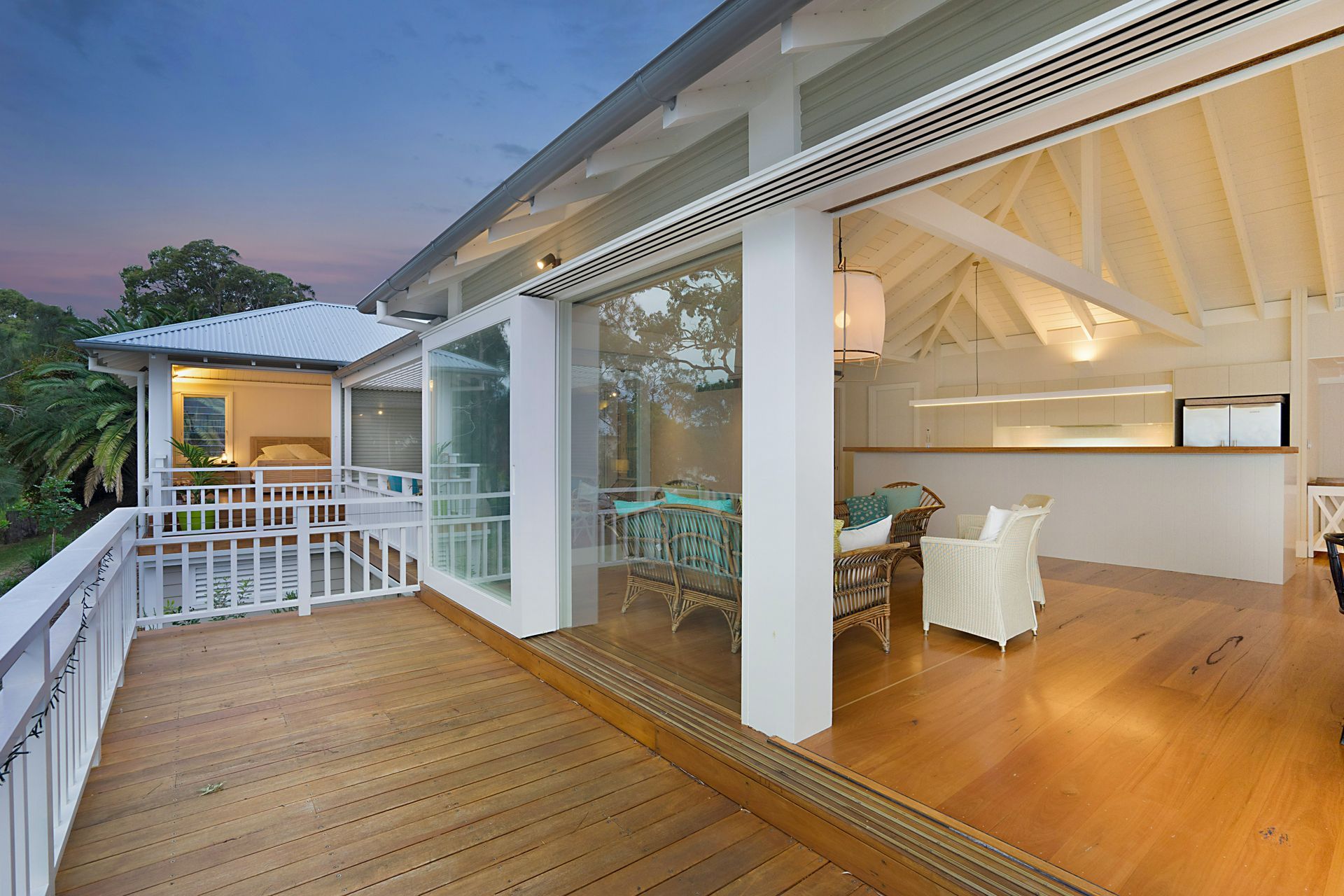 Wooden deck opens to a bright interior with glass sliding doors. White walls, wood floor, and furniture.