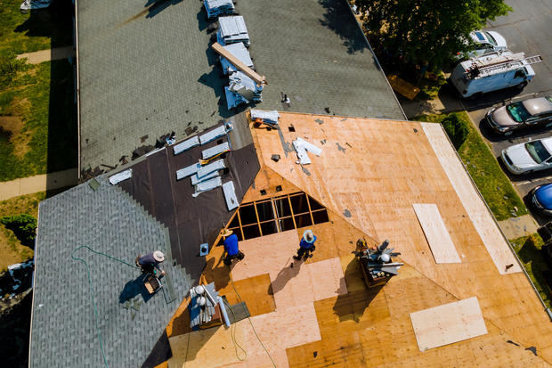 Roofers working on a house roof during replacement, with exposed plywood and shingles stacked nearby