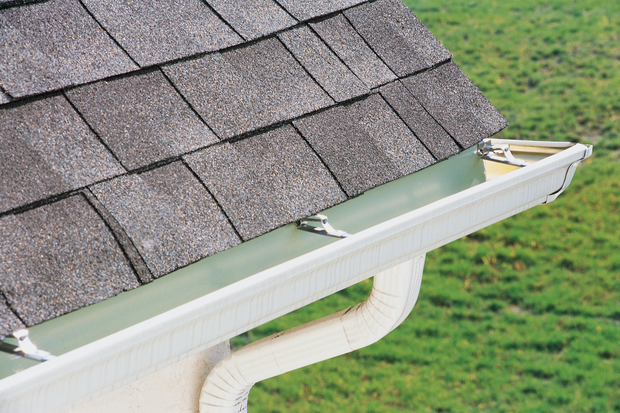 Gutter guard installed along a shingled roof edge, with green grass visible below
