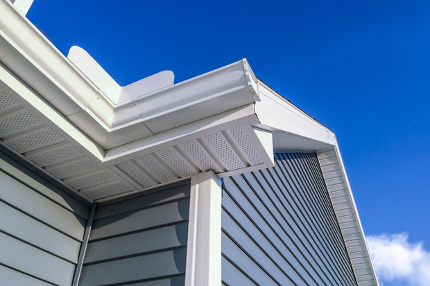 White house eave and gray siding against a bright blue sky with clouds