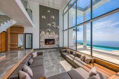 Modern living room with tall windows, gray seating, a fireplace, and ocean view