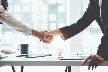 Two businesspeople shaking hands across a desk in a bright office
