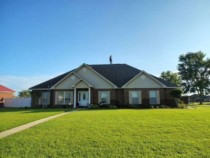 Single-story brick house with a large green lawn under a clear blue sky