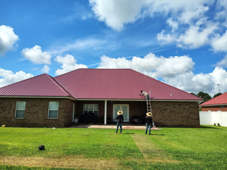 Brick house with red roof and two people on a green lawn under a blue sky