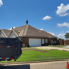 Suburban house with tiled roof, blue sky, and a large black dumpster in the driveway