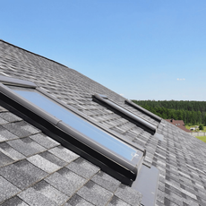 Rooftop skylights on a gray shingled roof under a clear blue sky.