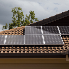 Solar panels mounted on a terracotta-tiled rooftop beneath a cloudy sky