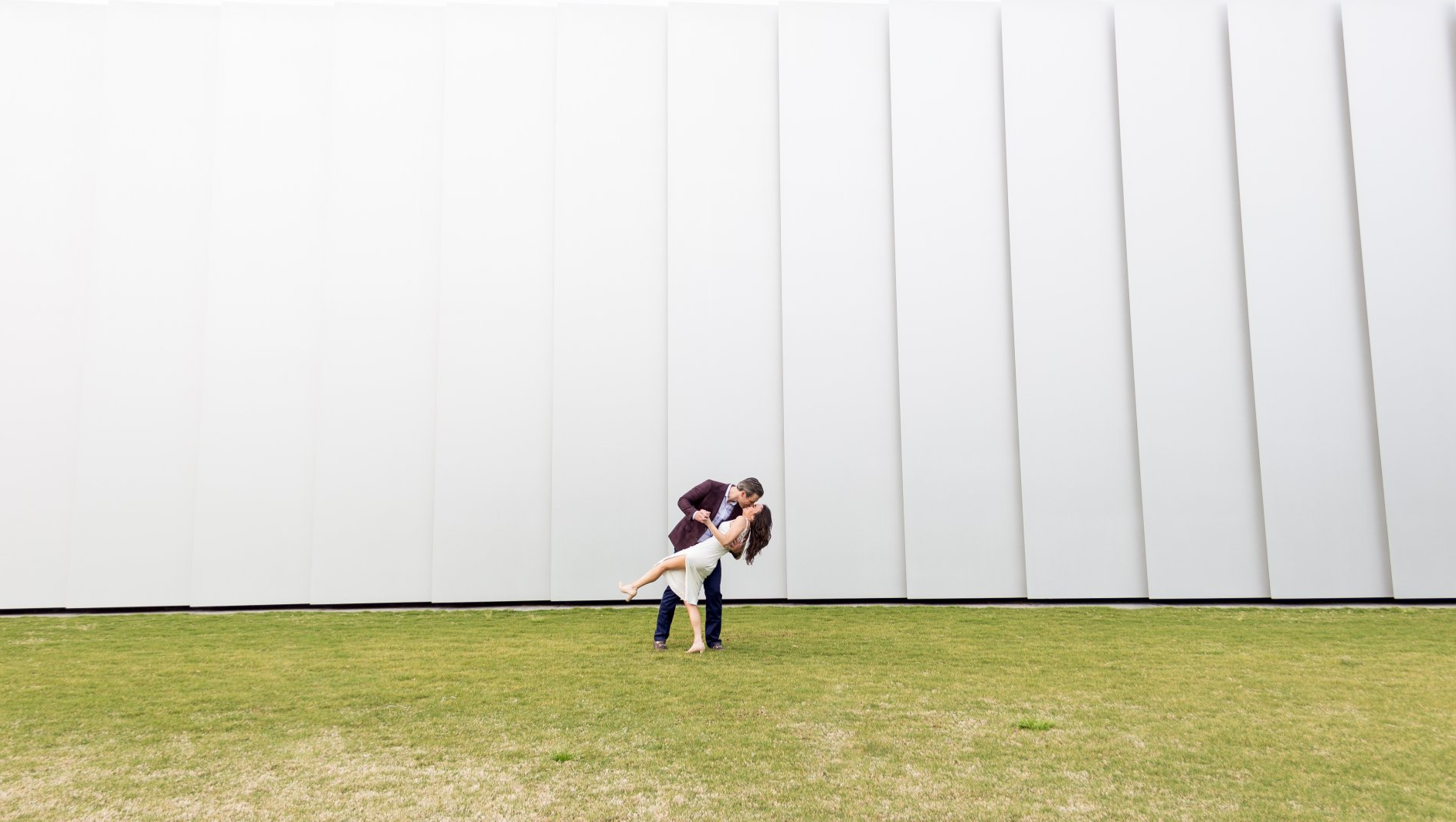 A man is holding a woman in his arms in front of a white wall.