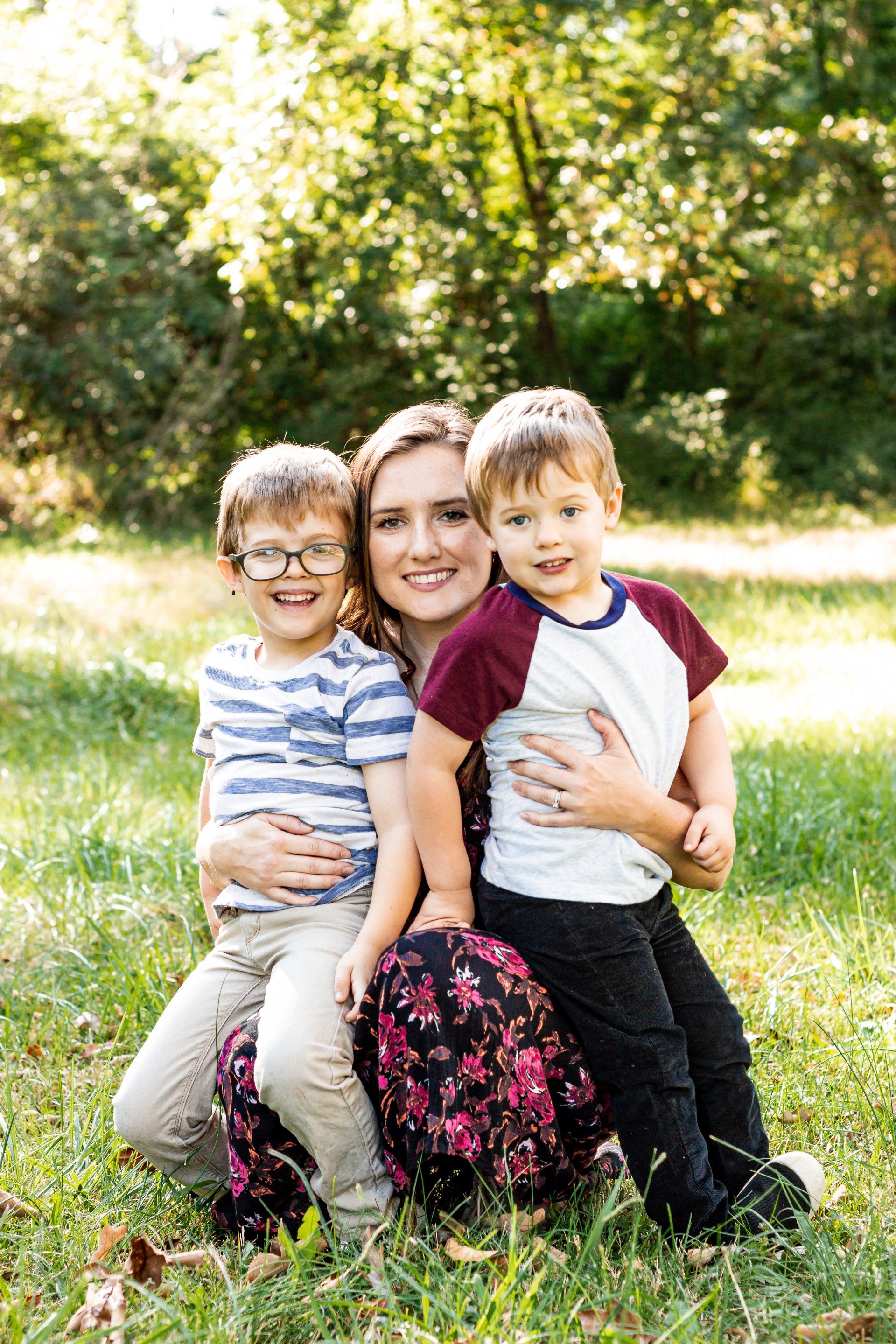 A woman is kneeling down with two children in the grass.