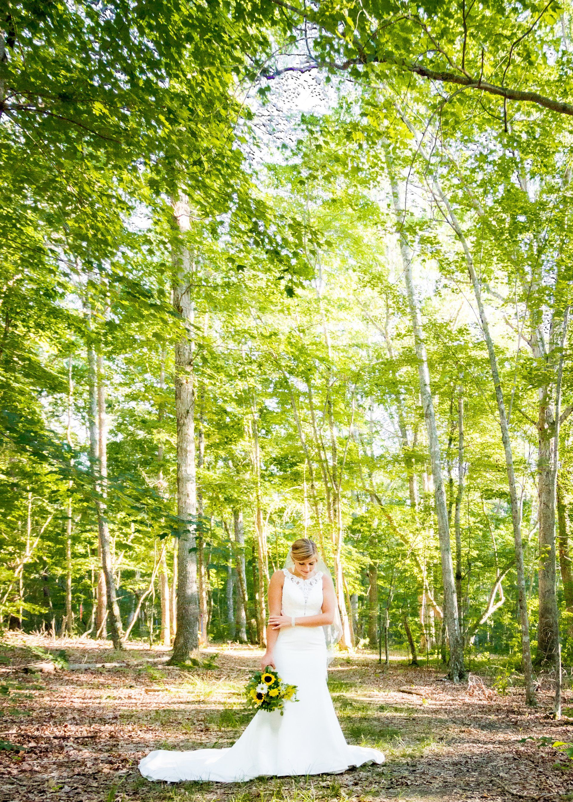 A bride in a wedding dress is standing in the middle of a forest holding a bouquet of flowers.