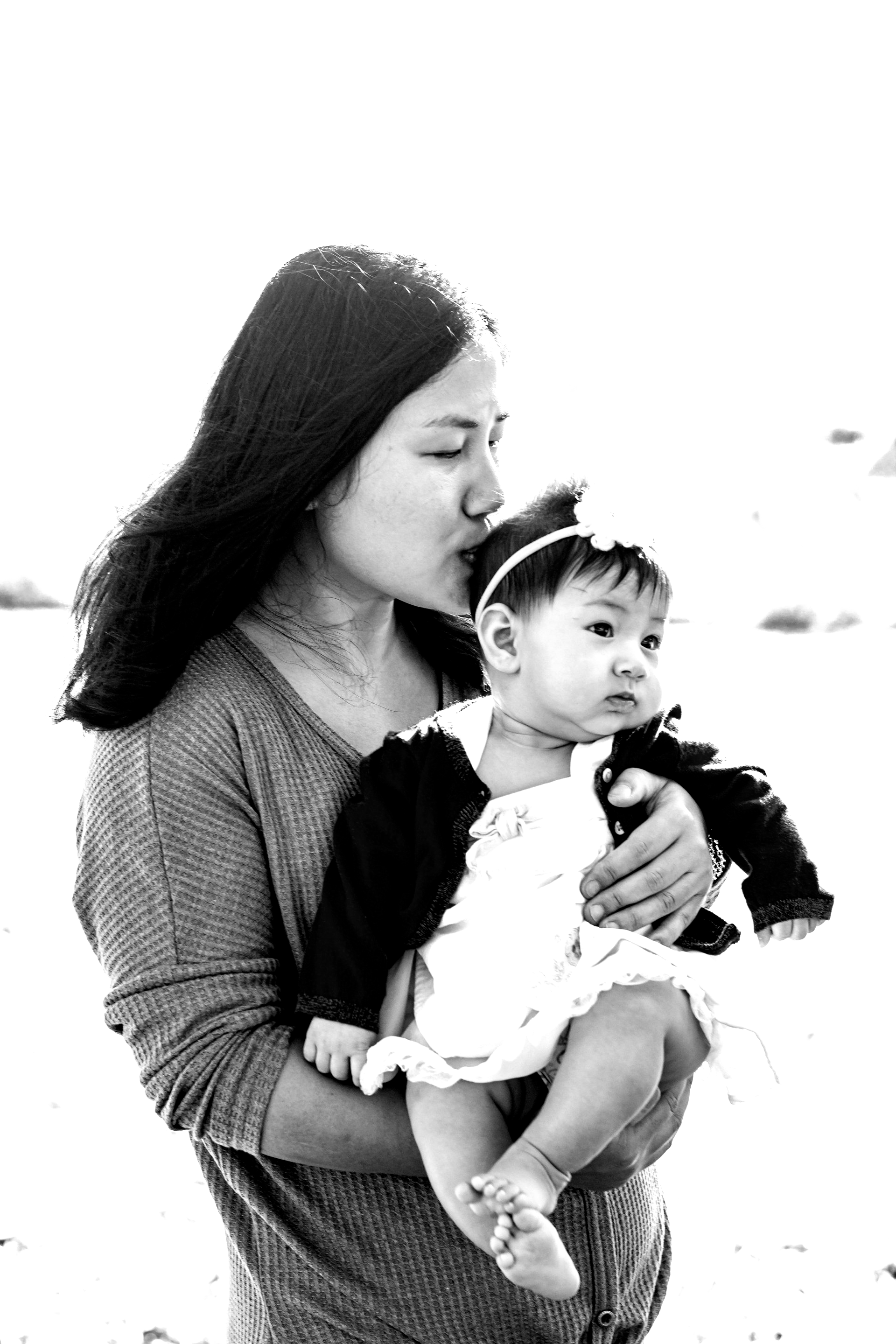 A woman is holding a baby in her arms and kissing it on the cheek.
