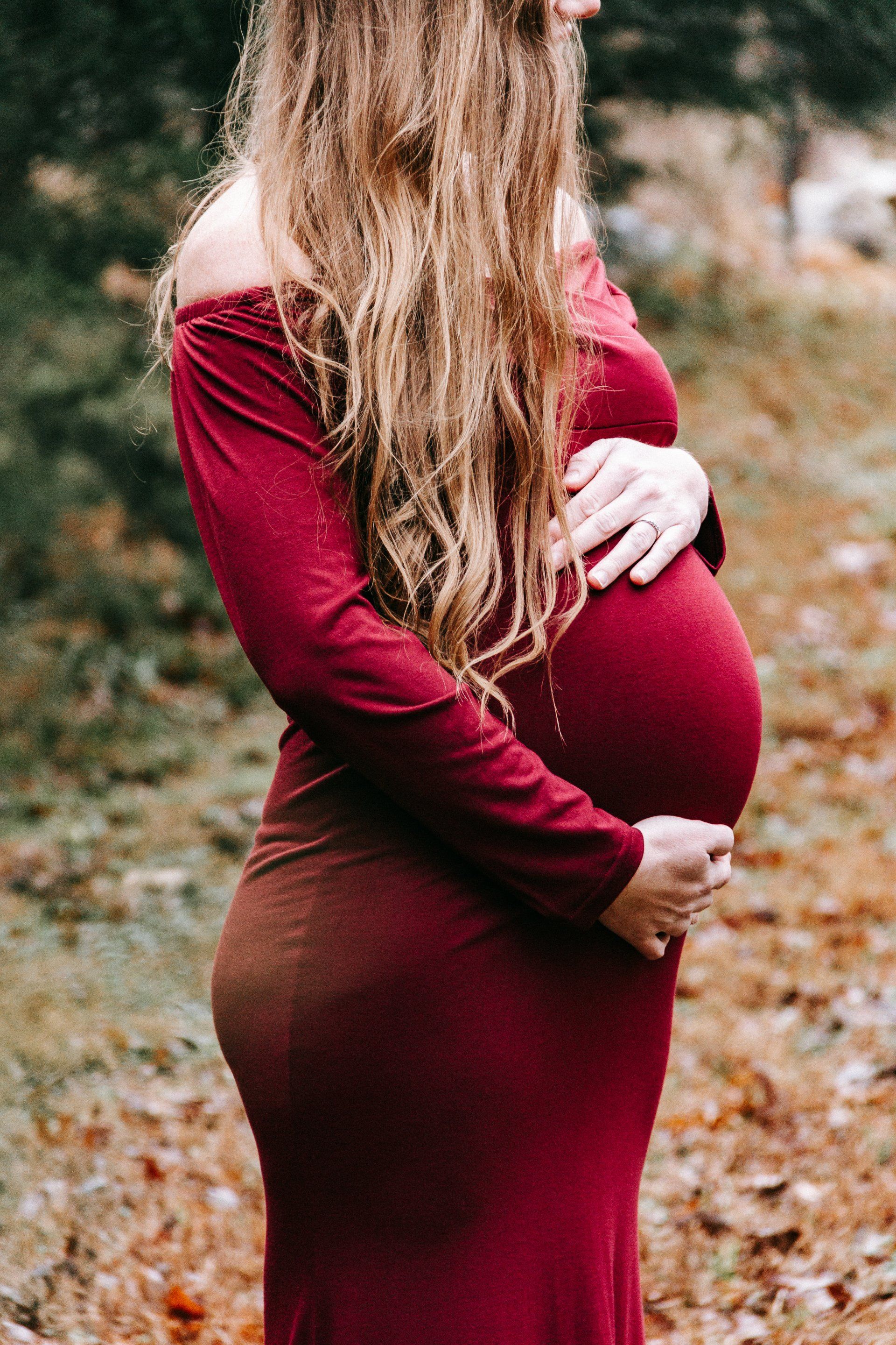 A pregnant woman in a red dress is holding her belly.