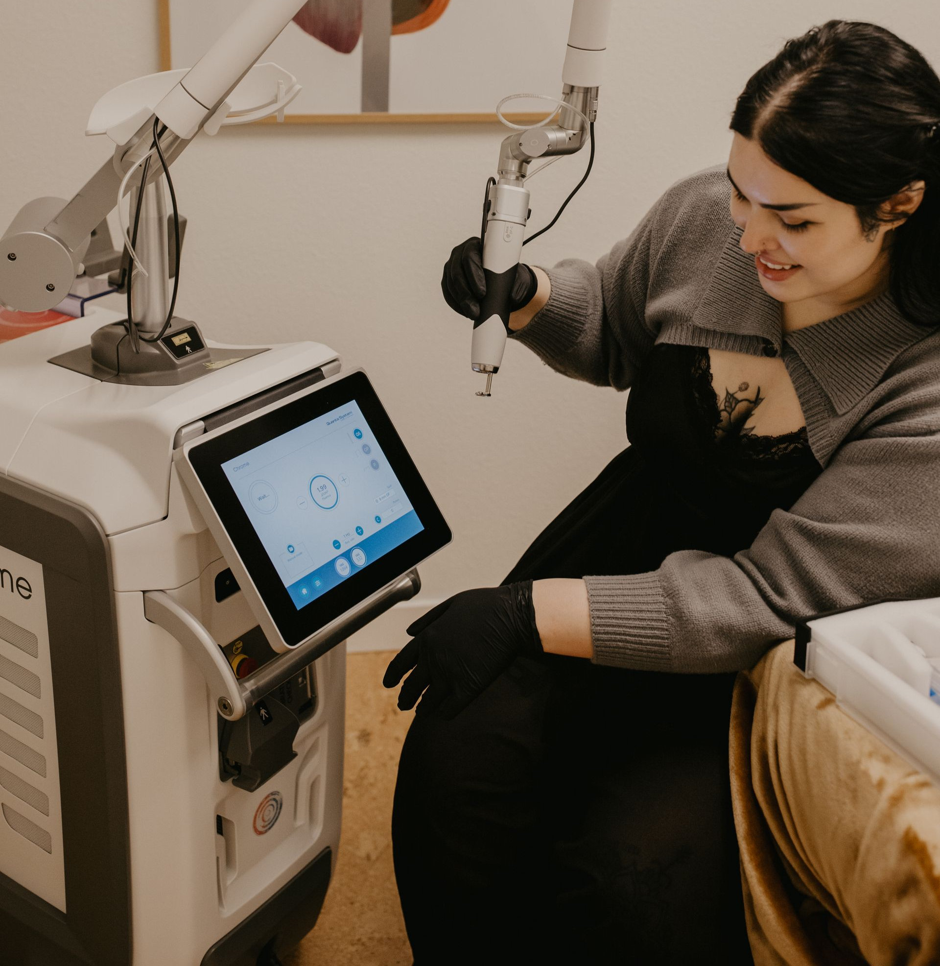 Person in a spa chair receives a facial treatment from a machine, smiling and holding the applicator.