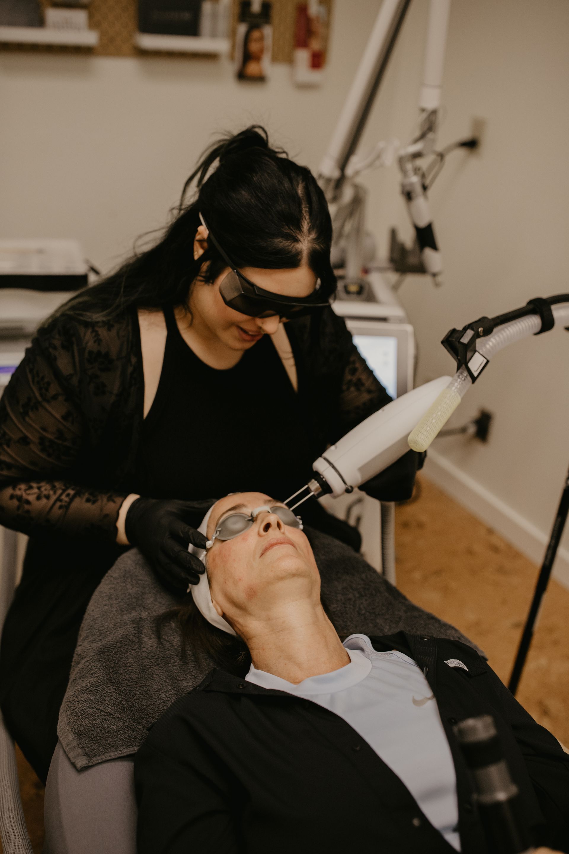 A professional performing a laser skin treatment on a client lying on a treatment table in a clinic.