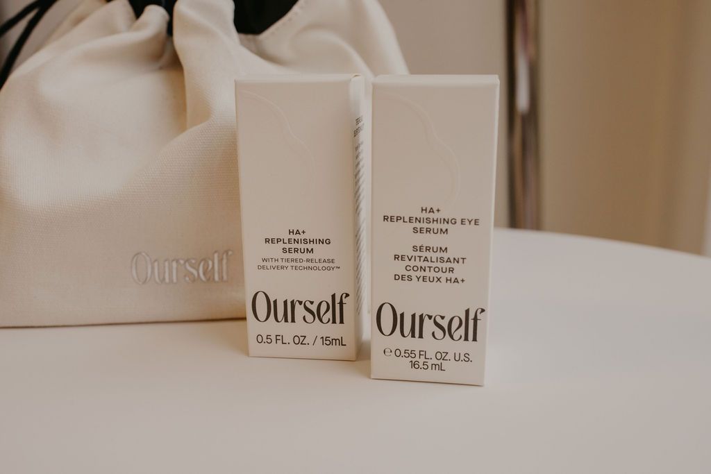 Two white perfume boxes on a beige table beside a cream handbag
