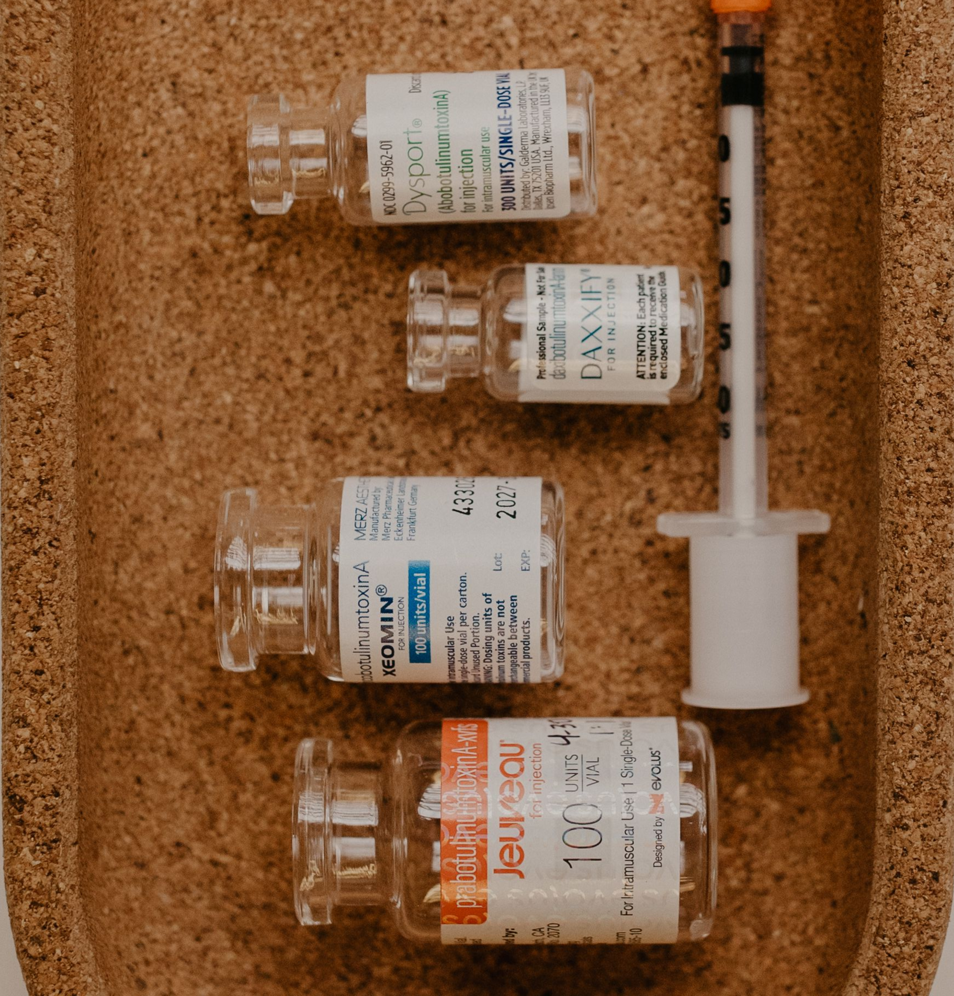 Four medicine vials and a syringe on a corkboard background