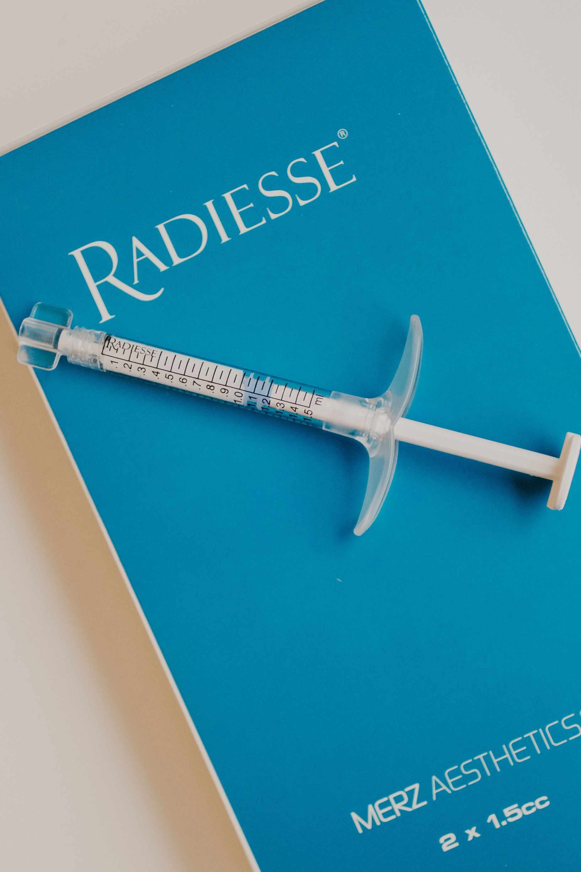 A Radiesse product box sits next to two syringes on an oval, textured cork tray.
