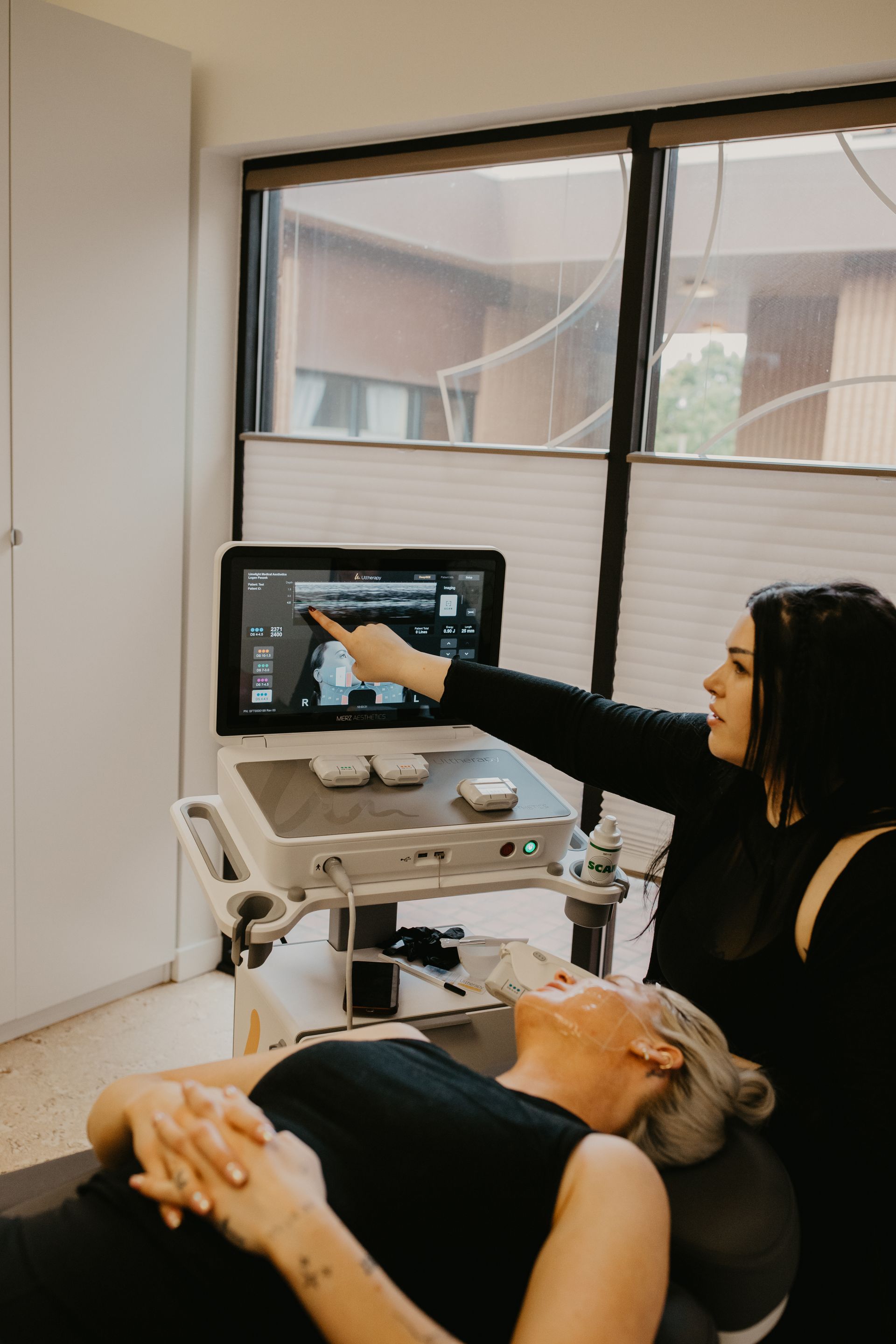 Ultrasound exam in clinic, with clinician pointing to a monitor beside a reclining patient.