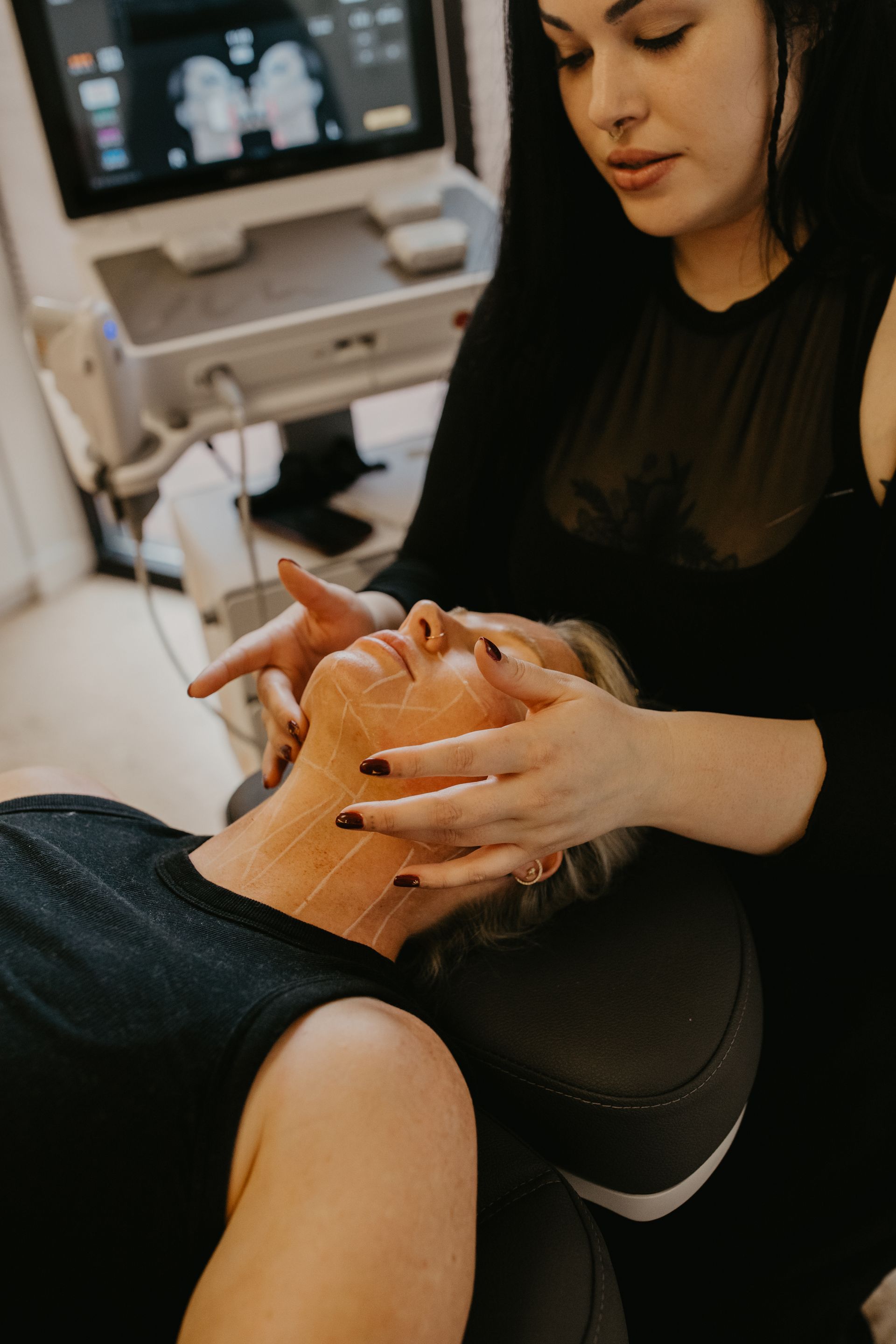 Woman administering a facial treatment to a client in a spa, with a monitor in the background