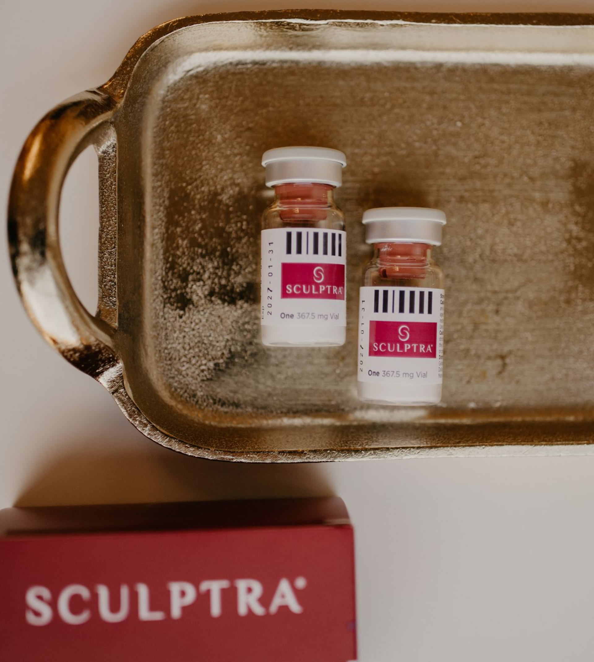 Two Sculptra vials on a gold tray with a red Sculptra box partially visible below