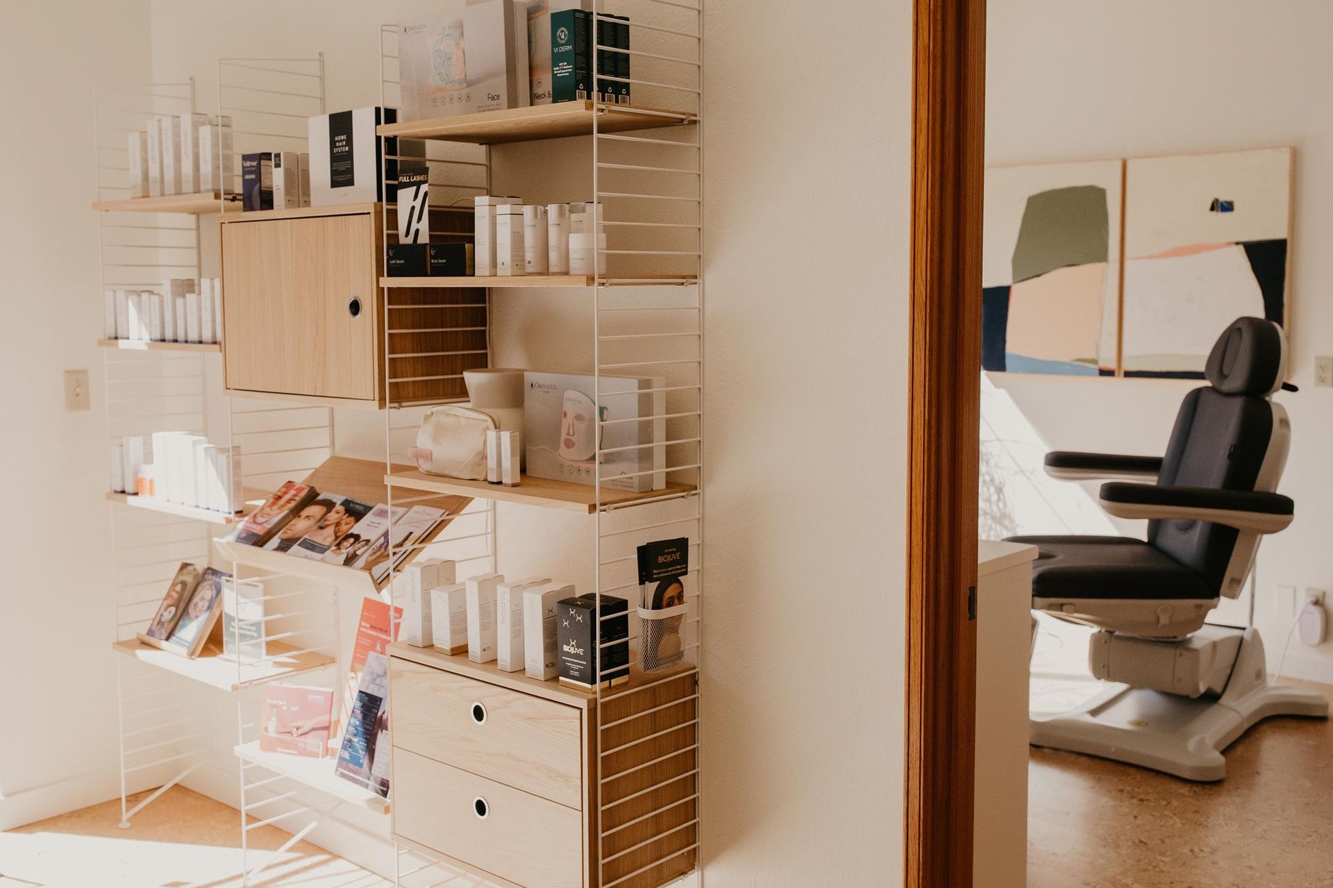 A room with a shelving unit displaying various products next to a professional reclining treatment chair.