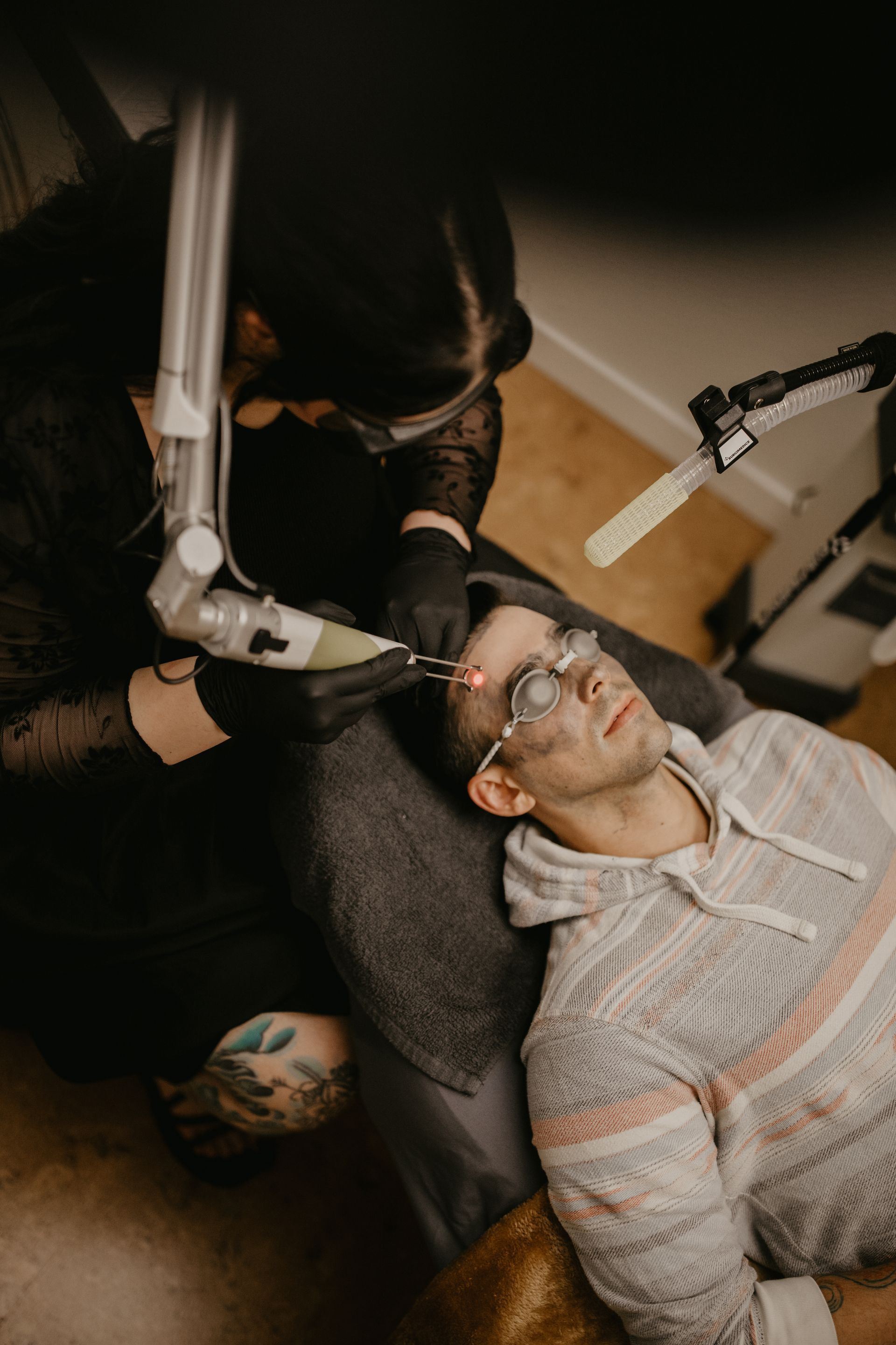 Person lying on a chair while a dental/medical tool is held near their face in a dim room
