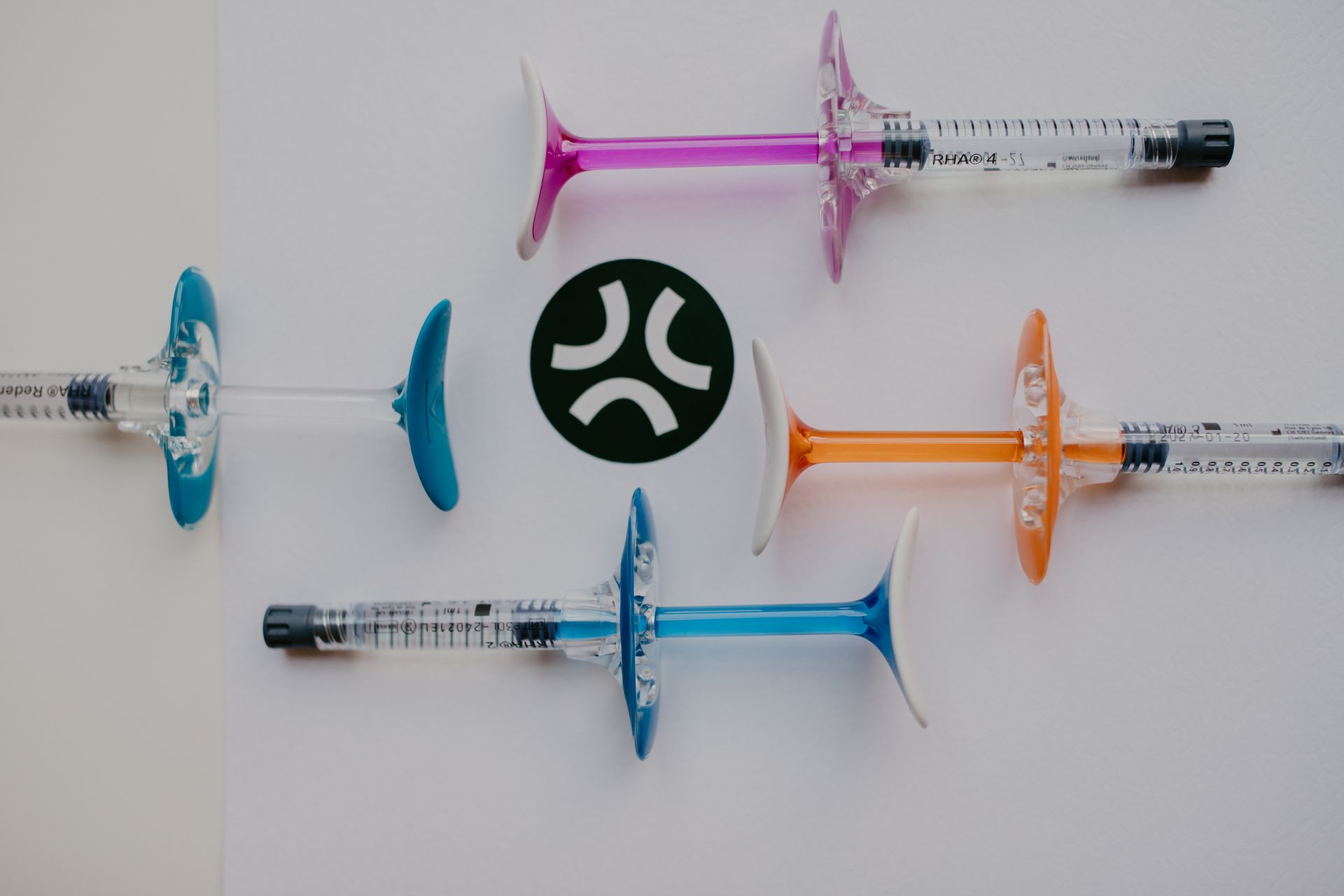 Colored syringes arranged around a black-and-green circular logo on a white background
