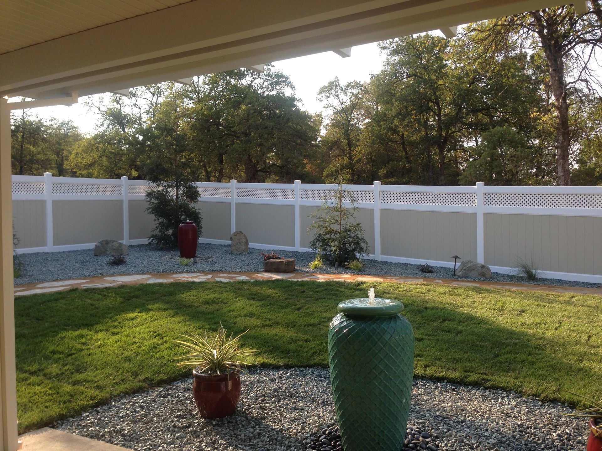 Backyard with green lawn, white fence, and large green ceramic pot under a covered patio