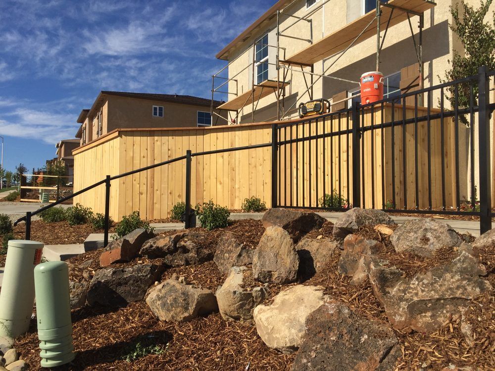 Rocky landscaped yard beside tan homes with a black fence and blue sky